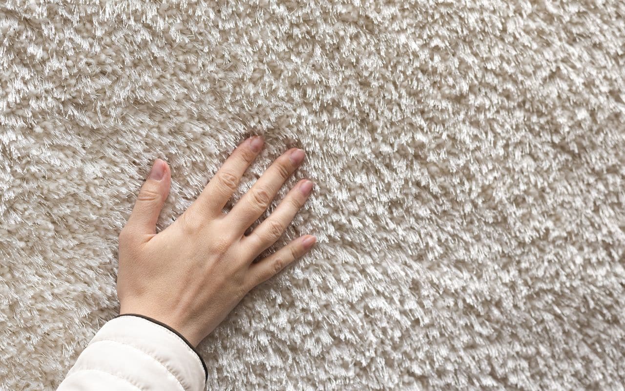 a texture of soft carpet flooring touch by right hand close up